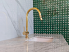 Unlacquered brass pull-down kitchen faucet installed at sink, bright finish