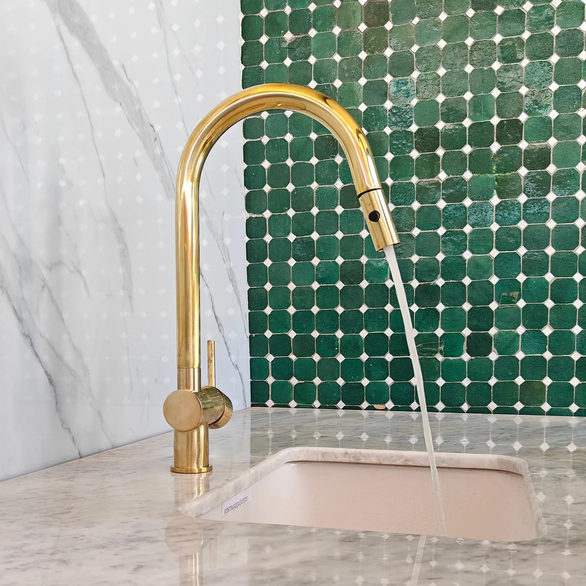 Unlacquered brass pull-down kitchen faucet installed at sink, bright finish