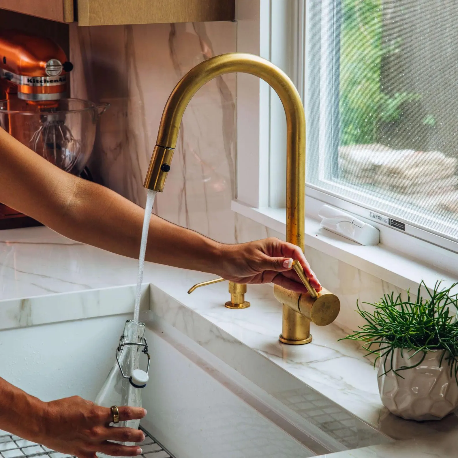 Unlacquered brass pull-down kitchen faucet installed at sink, bright finish