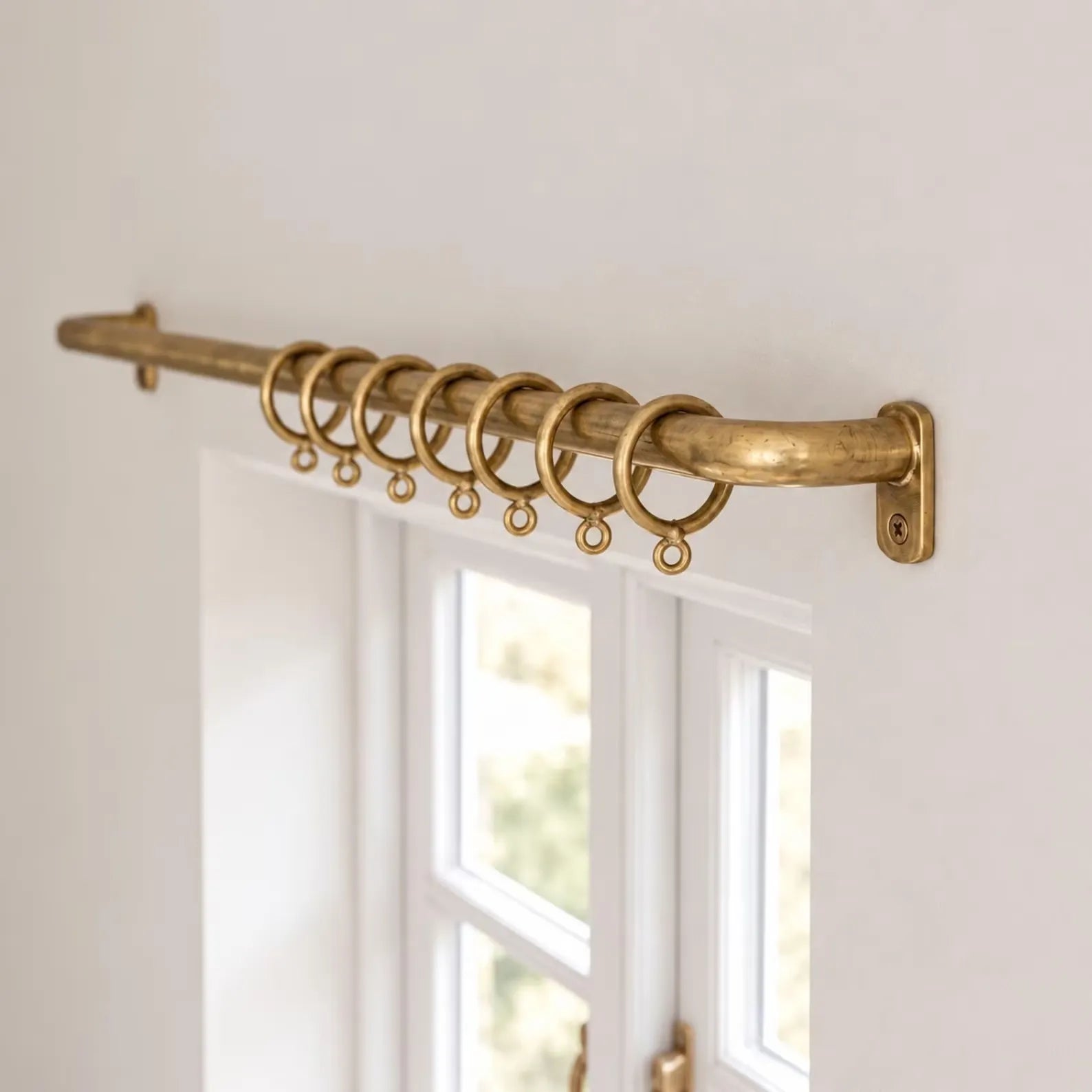Unlacquered brass French return curtain rod with rings installed above window
