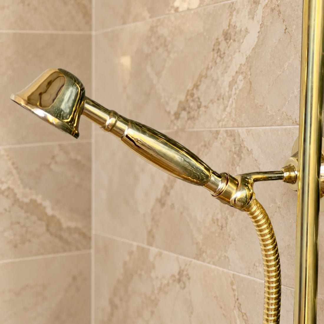 Unlacquered brass exposed thermostatic shower system with handheld shower installed on green and beige tiled bathroom wall