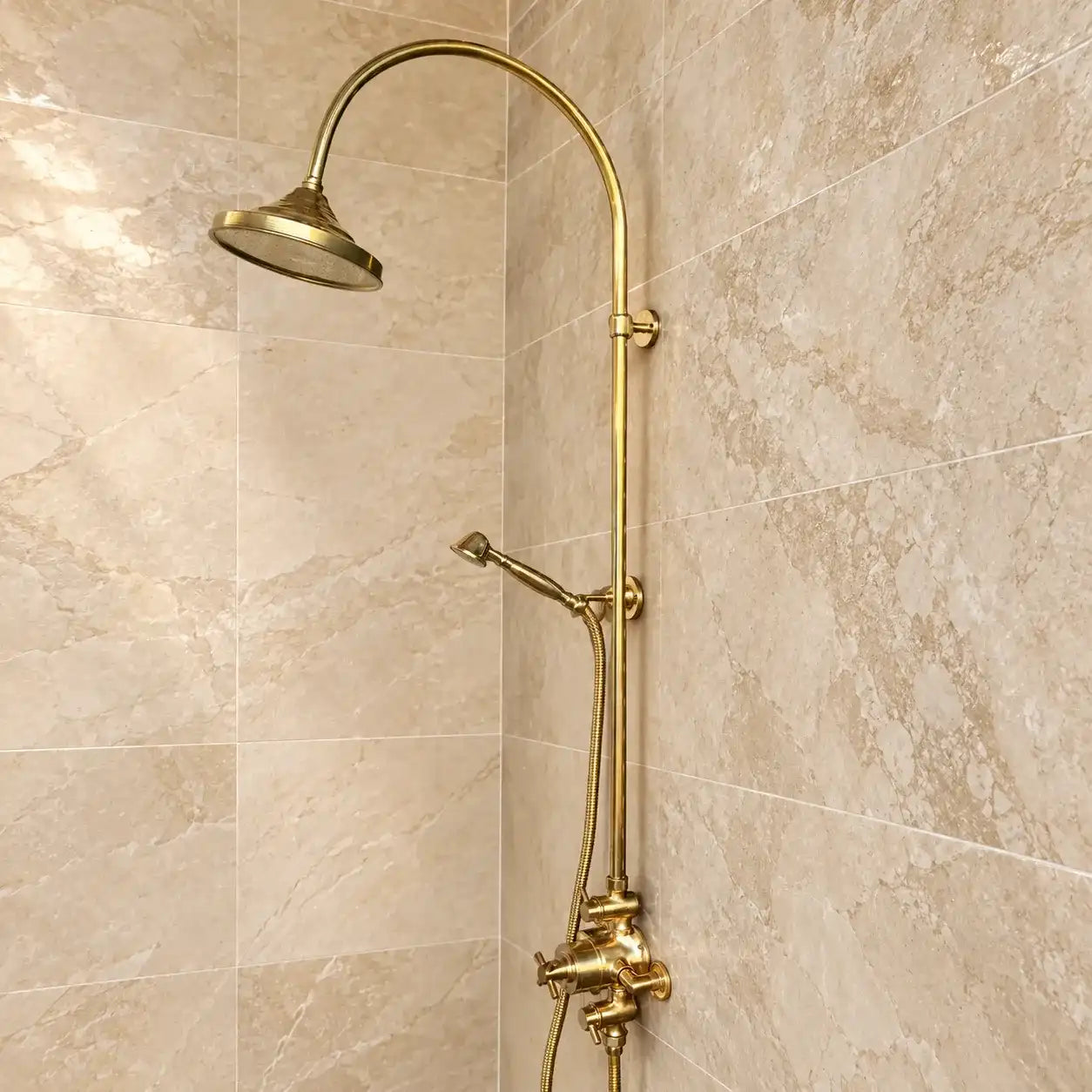 Unlacquered brass exposed thermostatic shower system with handheld shower installed on green and beige tiled bathroom wall